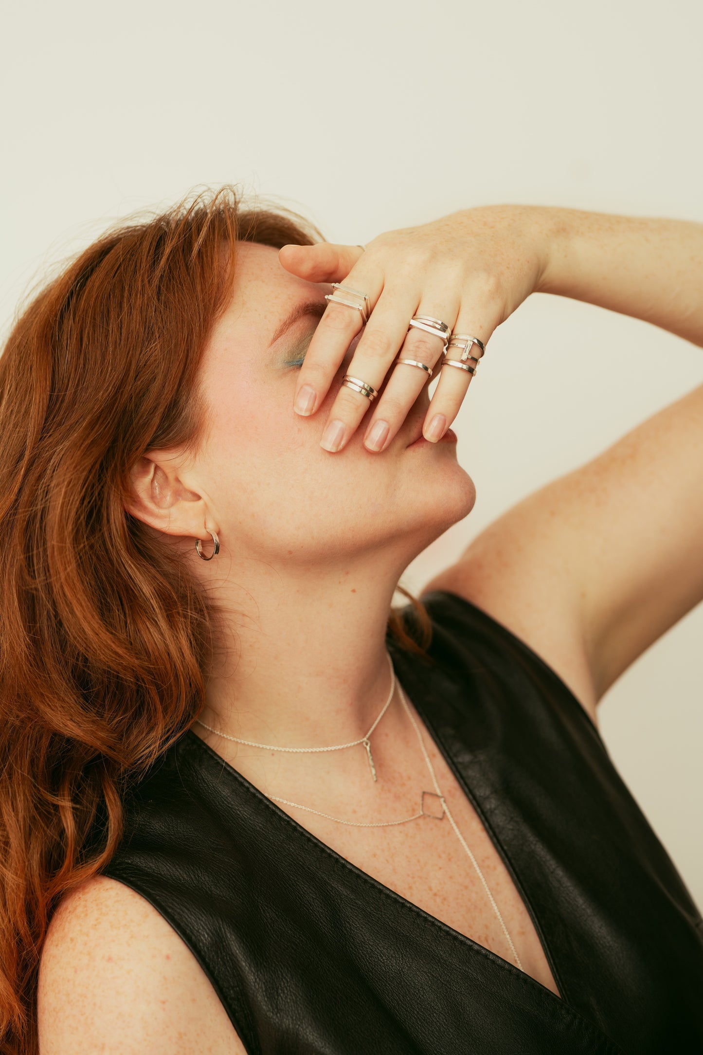 Woman with red hair wearing multiple rings and a necklace against a neutral background