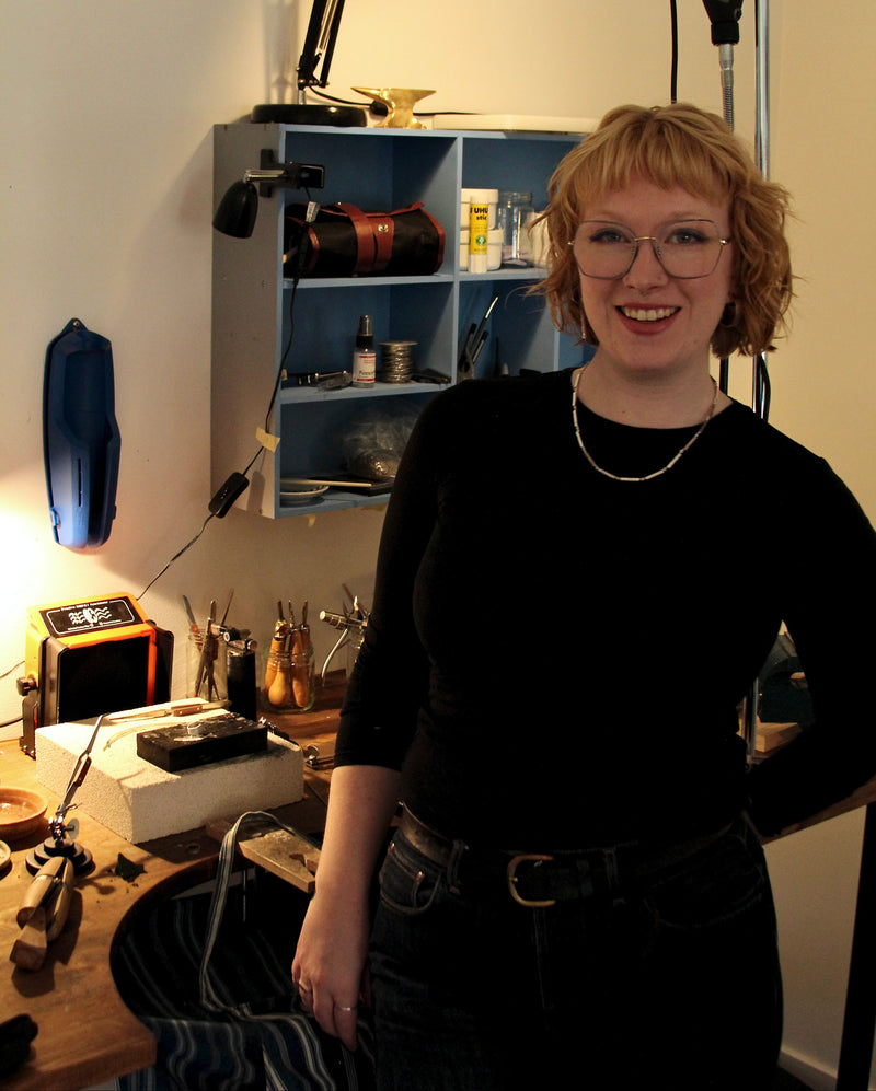 Frances Alexandra, standing in her jewellery workshop, surrounded by tools.