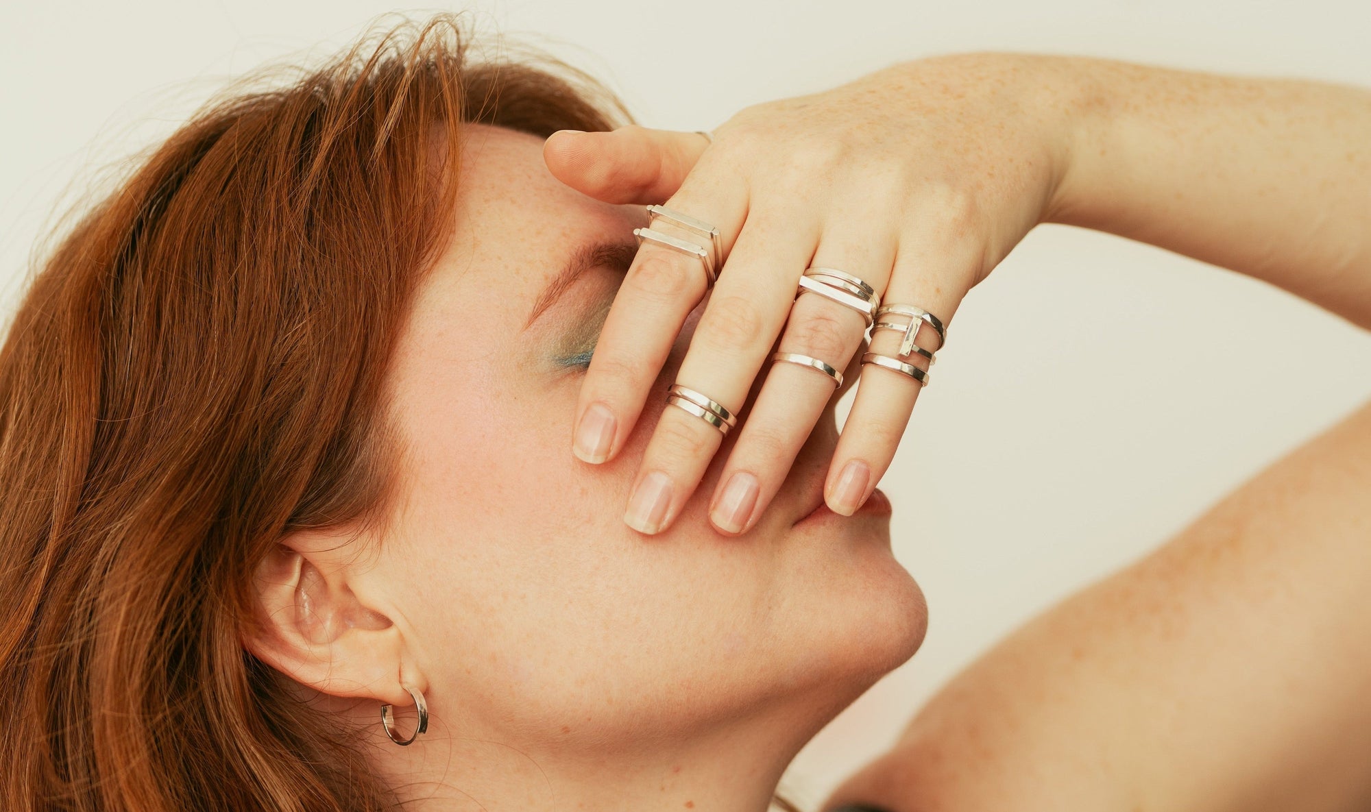 Woman with red hair wearing multiple rings and a necklace against a neutral background, wearing Frances Alexandra jewellery